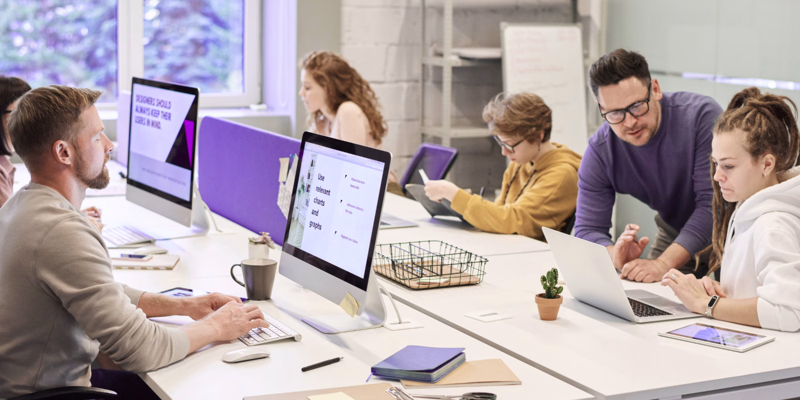 Creative team collaborating in a modern office with computers and laptops, focused on digital design and development tasks